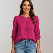 Woman wearing a pink blouse and blue jeans against a gray background