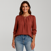 Woman wearing a rust-colored blouse and blue jeans on a gray background